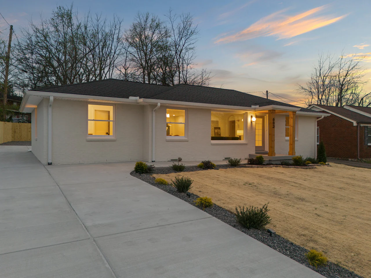 White brick home at dusk with a timber-framed entry porch and landscaped front yard