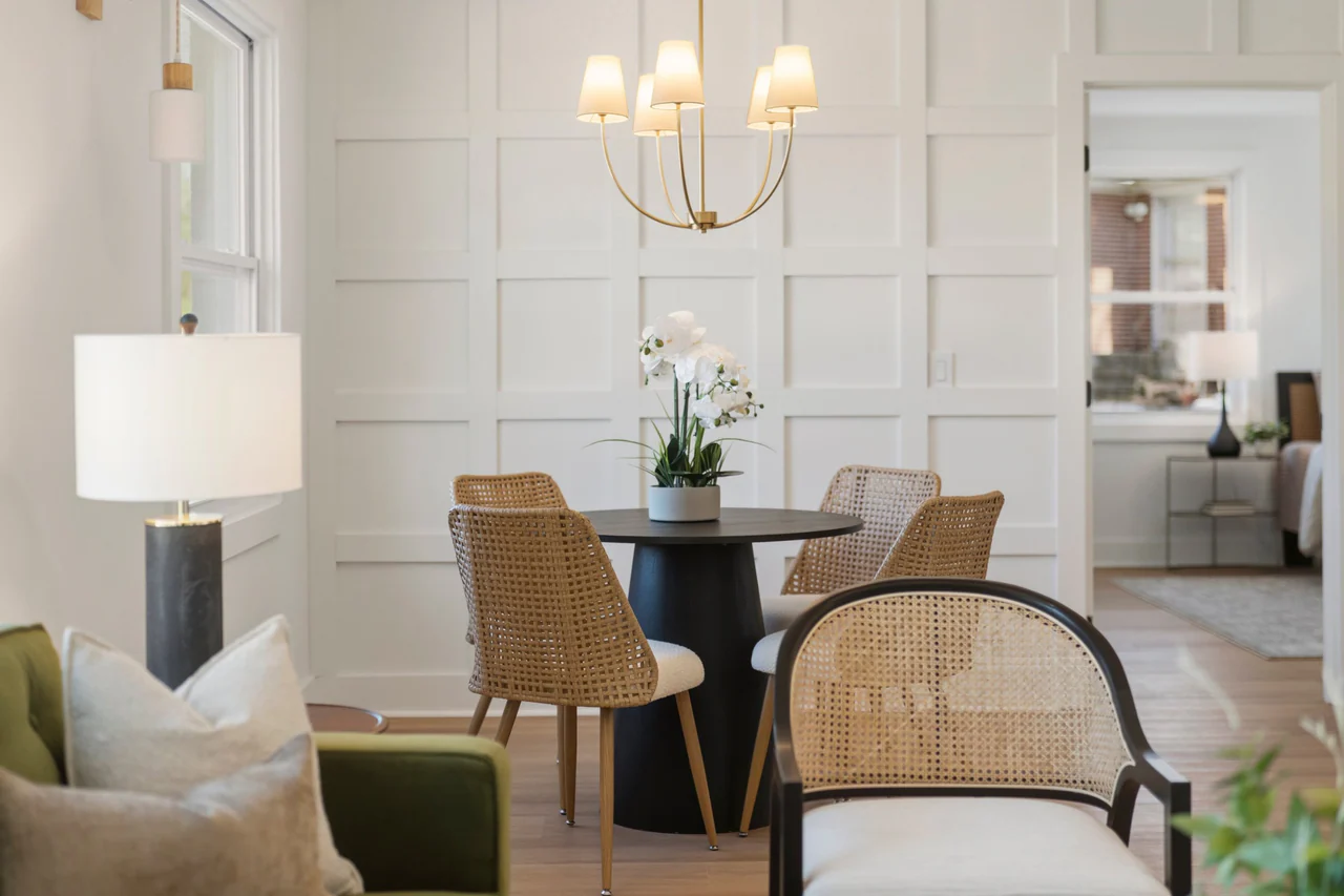 Dining area with round table, woven chairs and a paneled wall