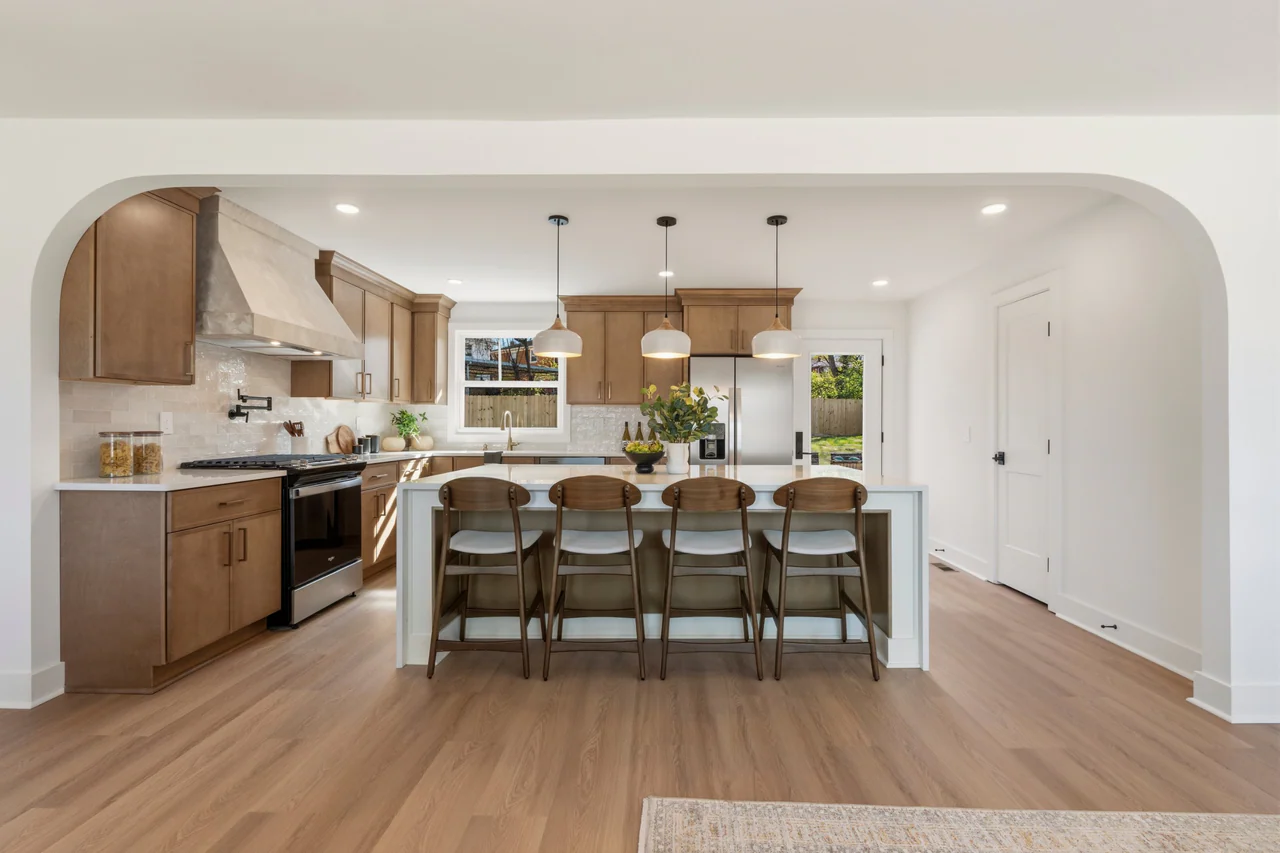 Kitchen framed by a wide arch, with island, stools and a plaster-finish range hood