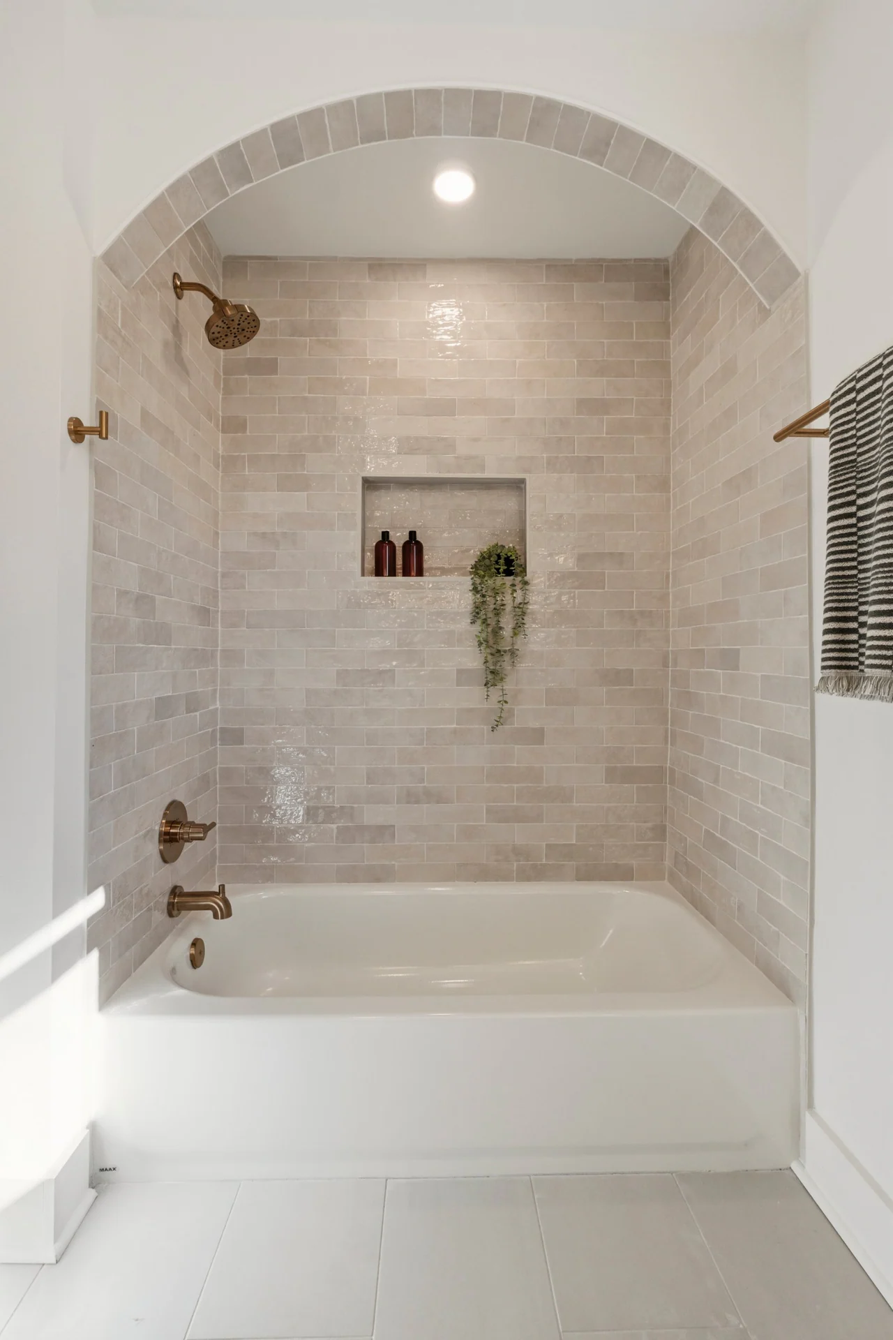 Arched tub alcove with glazed tile and brass fixtures
